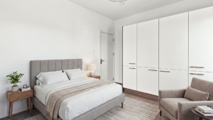 Reina Sophia Model Luca Unit 20 bedroom in Aruba with a grey upholstered bed, white bedding, built-in wardrobes, bedside tables, and a lounge chair.