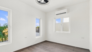 Reina Sophia Model Luca Unit 20 bedroom in Aruba with white walls, tiled flooring, multiple windows, and a wall-mounted air conditioner.