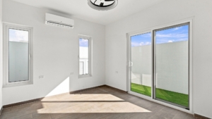 Reina Sophia Model Luca Unit 20 bedroom in Aruba with white walls, tiled floors, two windows, a wall-mounted air conditioner, and sliding glass doors opening toward a grassy outdoor area.