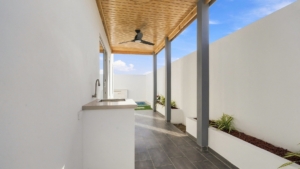 Covered outdoor area at Reina Sophia Model Luca Unit 20 in Aruba with a built-in counter and sink, tiled floor, wood ceiling, ceiling fan, and planted beds.