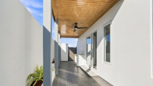 Covered outdoor patio at Reina Sophia Model Luca Unit 20 in Aruba with a wood ceiling, ceiling fan, tiled floor, white walls, and sliding glass doors.