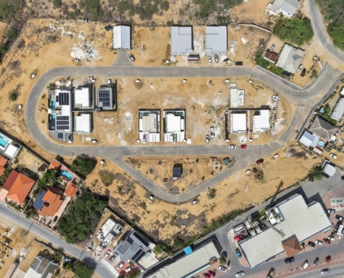 Top-down aerial view of the residential development around Reina Sophia Model Luca Unit 20 in Aruba showing roads, homes, open lots, and surrounding buildings.