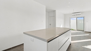 Reina Sophia Model Luca Unit 20 kitchen island in Aruba with a light countertop, white cabinetry, built-in electrical outlet, and open living area beyond.