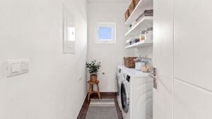 Reina Sophia Model Luca Unit 20 laundry room in Aruba with a front-loading washer and dryer, open shelving, storage containers, a small window, and tiled flooring.