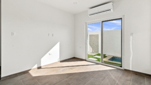 Reina Sophia Model Luca Unit 20 living room in Aruba with tiled flooring, a sliding glass door, and an outdoor area with a small pool visible beyond it.