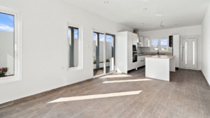 Reina Sophia Model Luca Unit 20 open interior in Aruba showing the kitchen island, sliding glass doors, windows, tiled floor, and white walls.