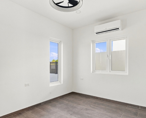 Reina Sophia Model Luca Unit 21 bedroom in Aruba with white walls, tiled flooring, multiple windows, and a wall-mounted air conditioner.