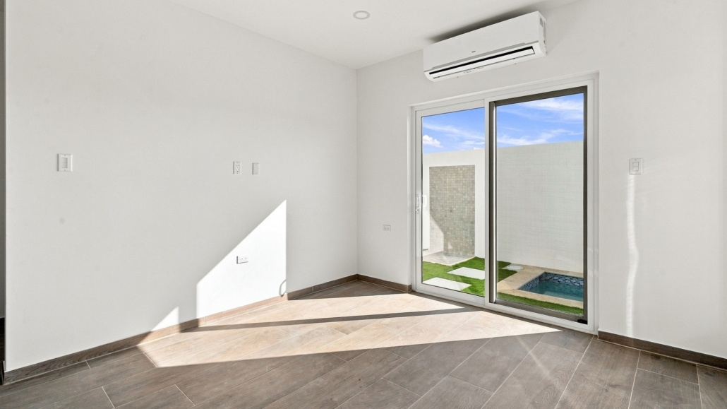 Reina Sophia Model Luca Unit 21 living room in Aruba with tiled flooring, a sliding glass door, and an outdoor area with a small pool visible beyond it.
