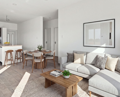 Staged Reina Sophia Model Luca Unit 21 open-plan interior in Aruba with a sectional sofa, coffee table, dining table, kitchen island, bar stools, and wall art.