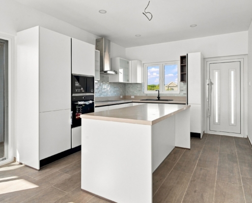 Reina Sophia Model Luca Unit 24 kitchen in Aruba with white cabinetry, a large island, built-in appliances, tiled backsplash, sink, and window.