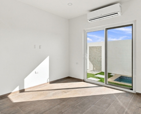 Reina Sophia Model Luca Unit 24 living room in Aruba with tiled flooring, a sliding glass door, and an outdoor area with a small pool visible beyond it.