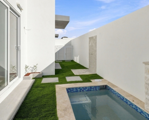 Private courtyard at Reina Sophia Model Luca Unit 24 in Aruba with a small rectangular pool, artificial grass, white walls, and large glass doors.