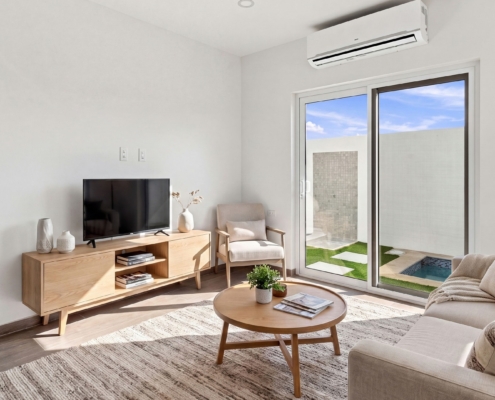 Staged Reina Sophia Model Luca Unit 24 living room in Aruba with a sofa, coffee table, television, armchair, rug, floor lamp, and sliding glass doors.