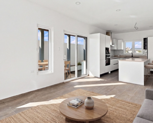 Staged Reina Sophia Model Luca Unit 24 interior in Aruba with a sofa, round coffee table, kitchen island, bar stools, dining chairs, and large windows