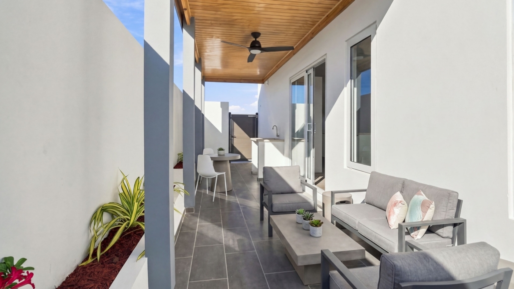 Furnished covered patio at Reina Sophia Model Luca Unit 25 in Aruba with gray outdoor seating, a coffee table, plants, tiled flooring, and a ceiling fan.