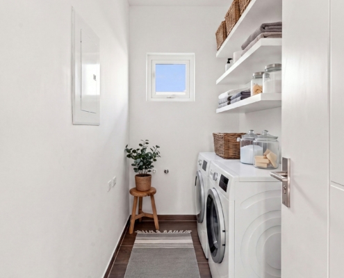 Reina Sophia Model Luca Unit 31 laundry room in Aruba with a front-loading washer and dryer, open shelving, storage containers, a small window, and tiled flooring.