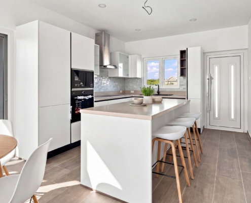 Staged Reina Sophia Model Luca Unit 31 kitchen in Aruba with white cabinets, a large island, bar stools, dining table, appliances, and backsplash