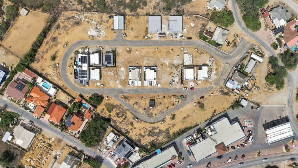 Reina Sophia Model Luca Unit 32 Development Aerial View in Aruba Top-down aerial view of the residential development around Reina Sophia Model Luca Unit 32 in Aruba showing roads, homes, open lots, and surrounding buildings.