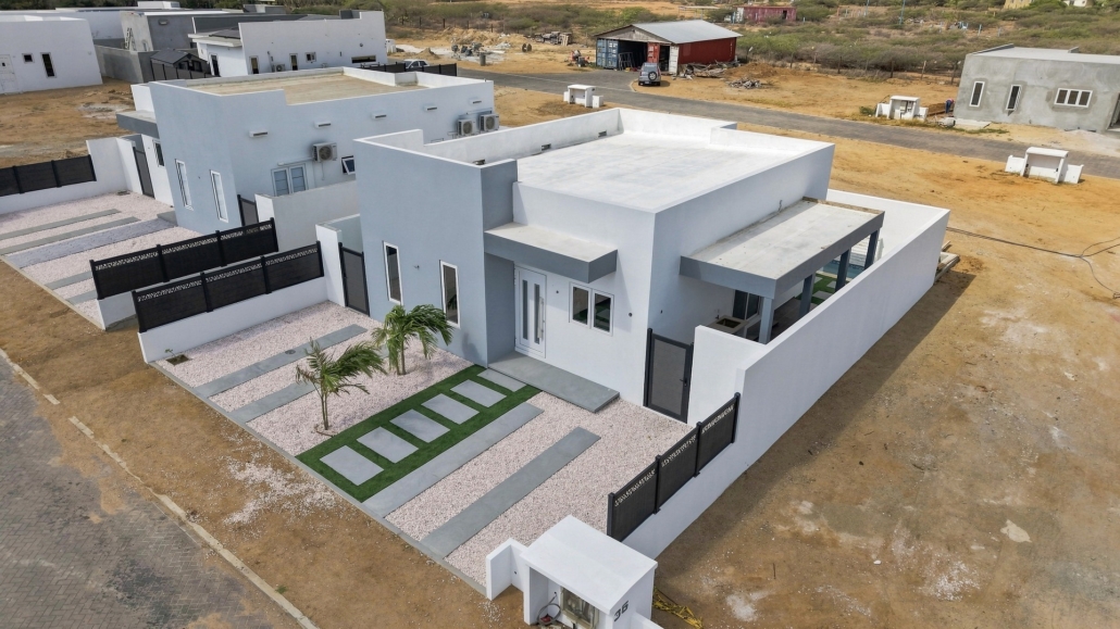 Aerial exterior view of Reina Sophia Model Luca Unit 35 in Aruba showing the white building, enclosed outdoor spaces, front landscaping, and surrounding neighborhood.