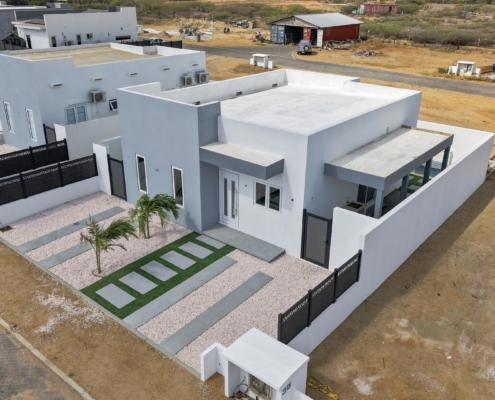 Reina Sophia Model Luca Unit 36 Aerial Exterior in Aruba Aerial exterior view of Reina Sophia Model Luca Unit 36 in Aruba showing the white building, enclosed outdoor spaces, front landscaping, and surrounding neighborhood.
