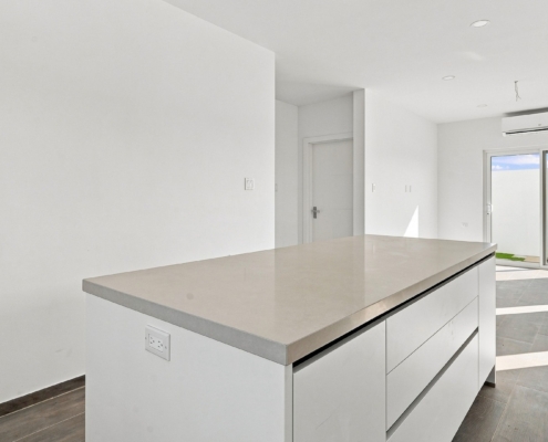 Kitchen island detail at Luca Unit 36 Aruba Reina Sophia Model Luca Unit 36 kitchen island in Aruba with a light countertop, white cabinetry, built-in electrical outlet, and open living area beyond.